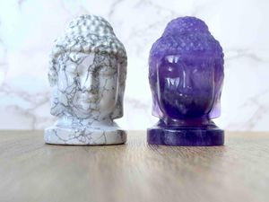 crystal buddha heads in white howlite and purple fluorite standing beside each other