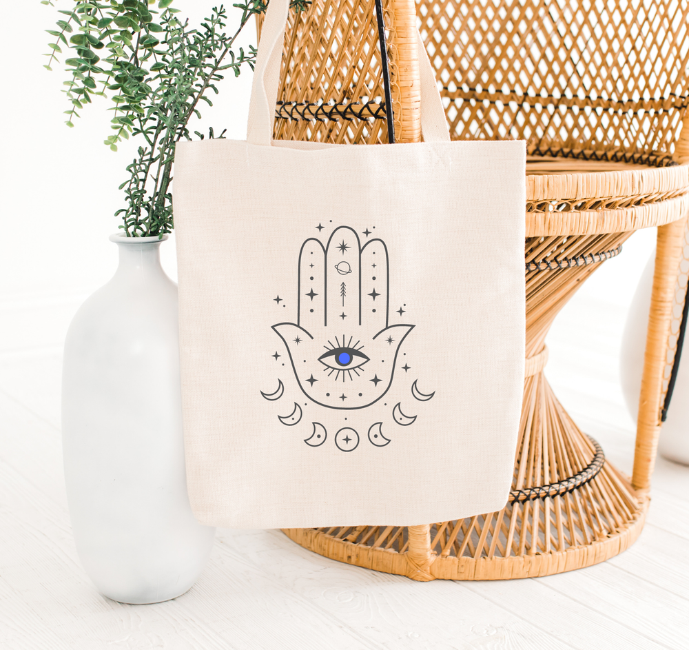 hamsa hand tote bag with evil eye hanging on a chair, the holistic hamper