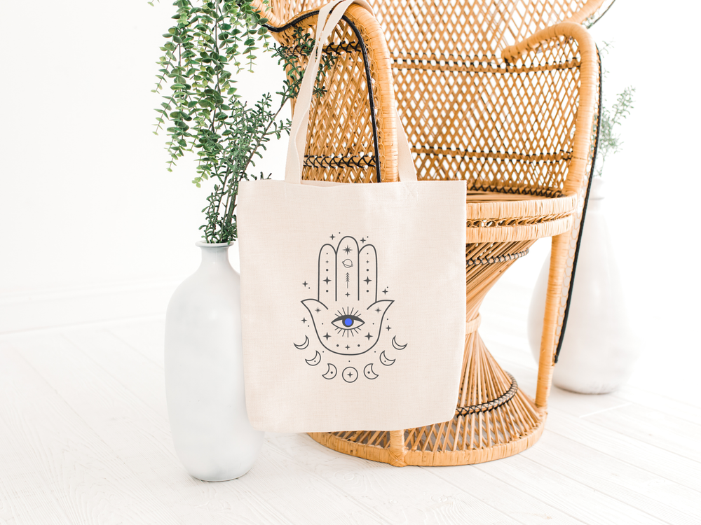hamsa hand tote bag with evil eye hanging on a chair, the holistic hamper