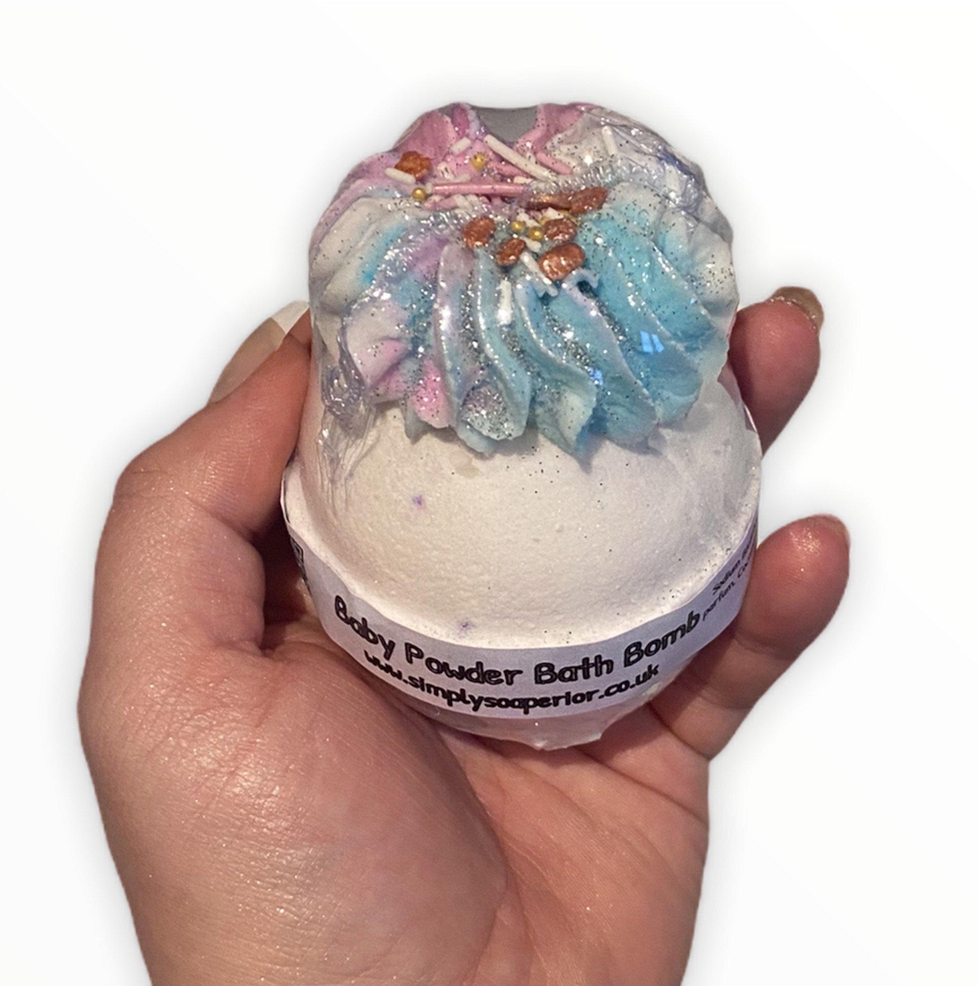 A  designer Baby Powder bath bomb encased with minimal shrink-wrap packing, displaying the label of the product.
