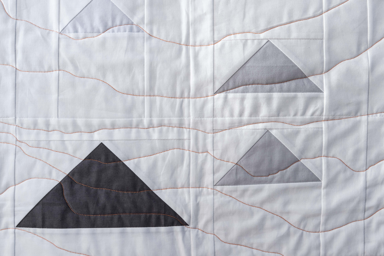 Decorative close up photograph of Monadh quilt showing white background and flying geese in varying shades of grey