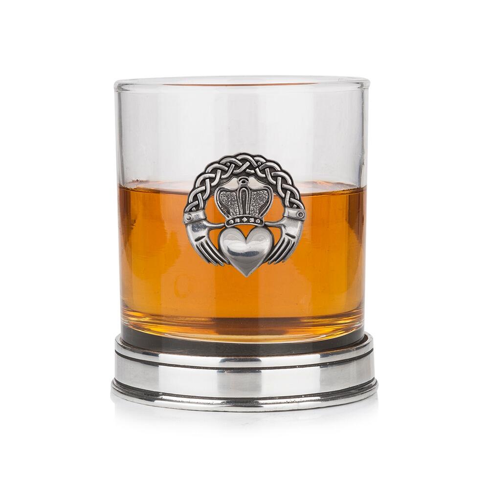 Whisky tumbler with pewter Claddagh motif featuring crown, heart and hands, with polished base, partially filled with amber liquid