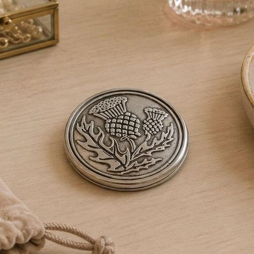 Round pewter compact purse mirror featuring an intricate traditional Scottish thistle design with textured leaves and cross-hatched flower heads