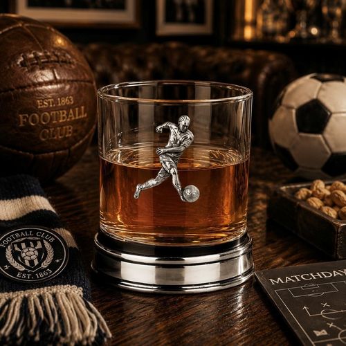 Whisky tumbler with pewter footballer emblem and polished base, partially filled with amber liquid