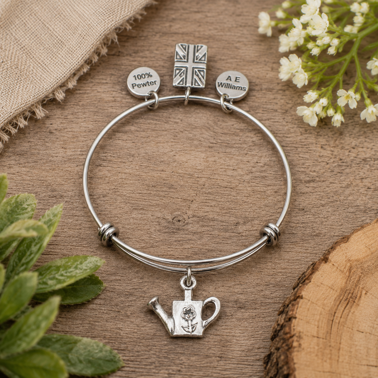 Pewter watering can charm expandable bracelet with 100% Pewter and A E Williams tags displayed in a rustic garden-inspired lifestyle setting