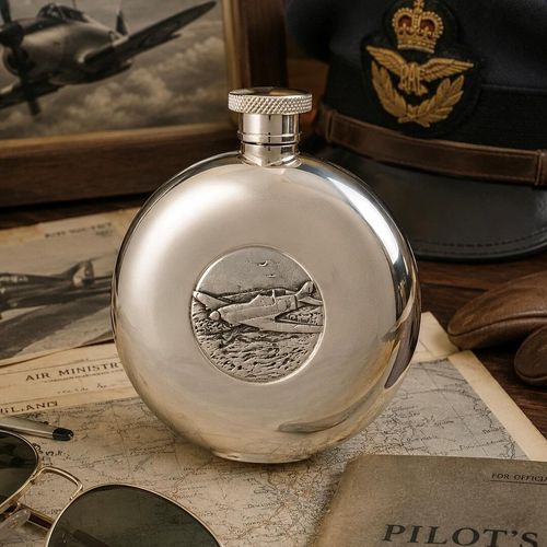 Polished round pewter hip flask featuring a central medallion embossed with a Hawker Hurricane fighter aircraft, set on vintage navigation maps alongside an RAF officer cap and aviator sunglasses