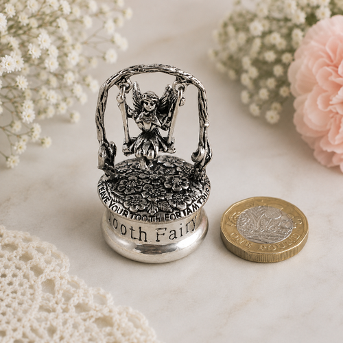 Small pewter tooth fairy keepsake box featuring a fairy on a swing above a floral lid, displayed beside a £1 coin to show scale.
