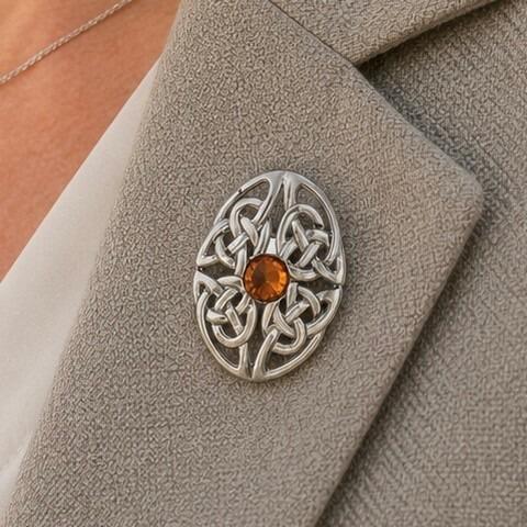 An oval pewter brooch featuring intricate openwork Celtic knotwork and a central faceted amber-colored stone
