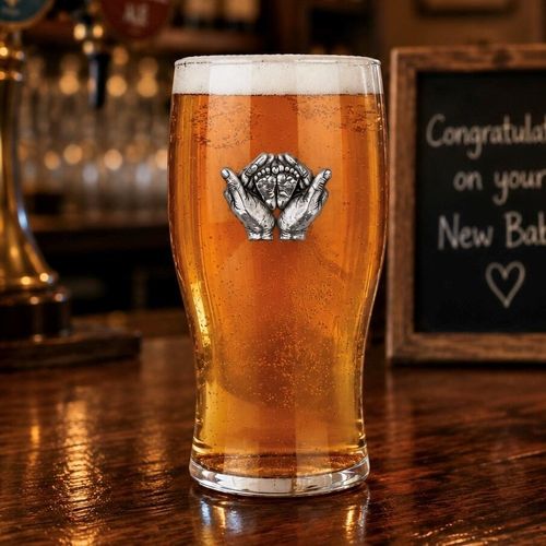Pint glass with handmade pewter “New Baby” badge, filled with golden beer