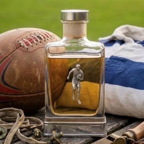 A glass flask with a pewter base and a handcrafted pewter rugby emblem on the front