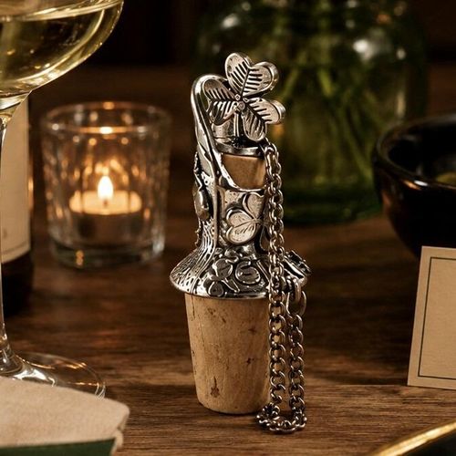 Pewter wine pourer and cork stopper featuring a sculpted traditional Irish shamrock top and engraved clover designs, displayed on a wooden table beside a glass of white wine and a lit candle