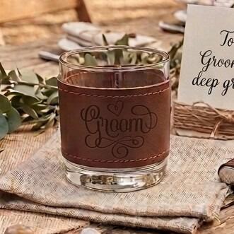 Glass tumbler wrapped in a brown stitched leather sleeve engraved with the word "Groom" and a small heart