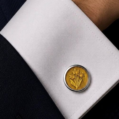 A circular pewter cufflink featuring an embossed bunch of daffodil flowers on a vibrant yellow enameled background