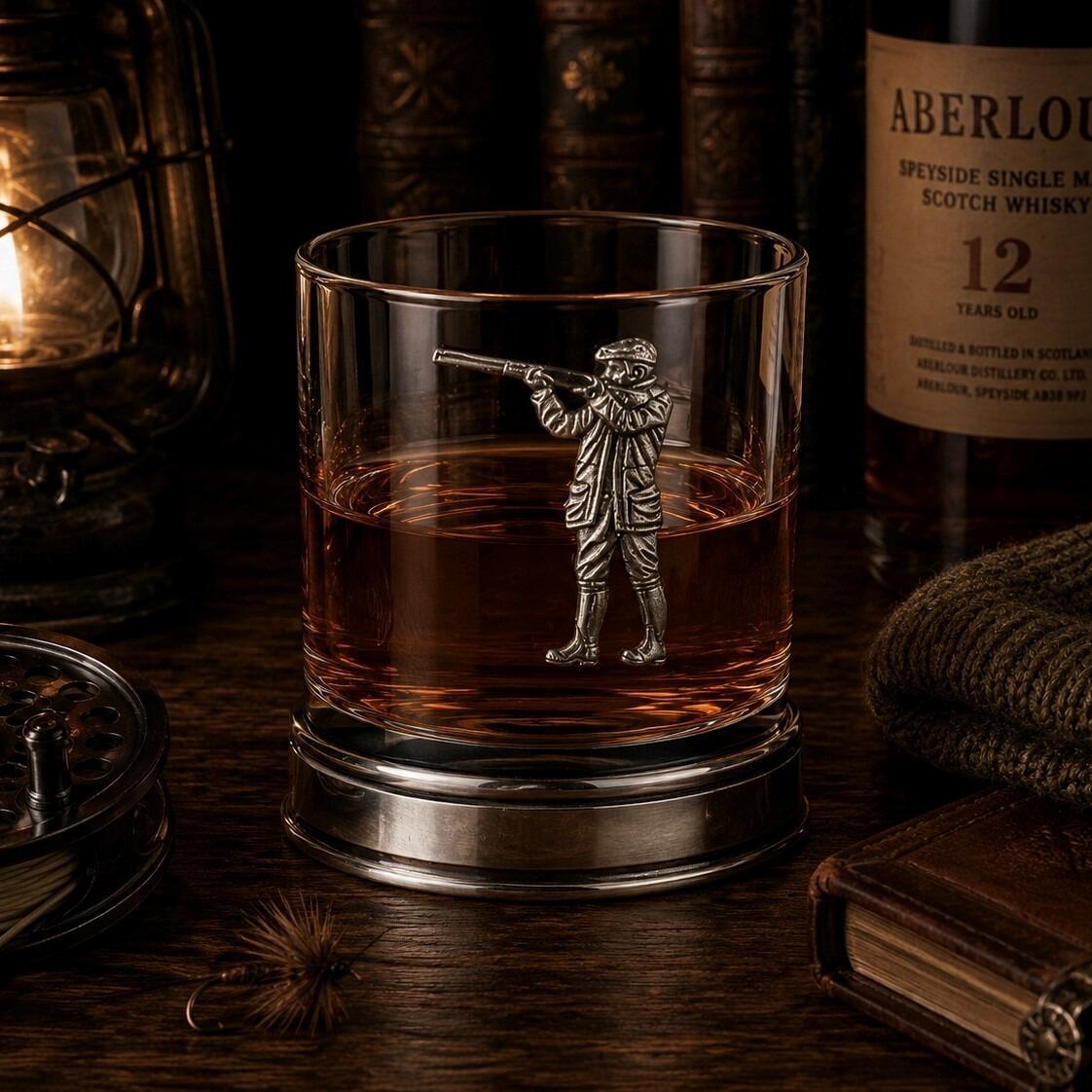 Whisky tumbler with pewter shooting motif and polished base, partially filled with amber liquid