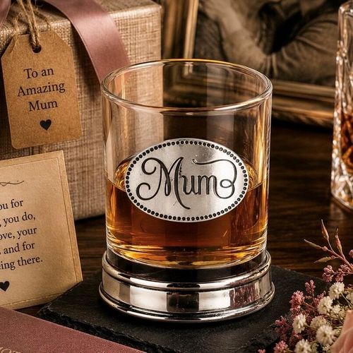 Whisky tumbler with pewter 'Mum' badge and polished base, partially filled with amber liquid