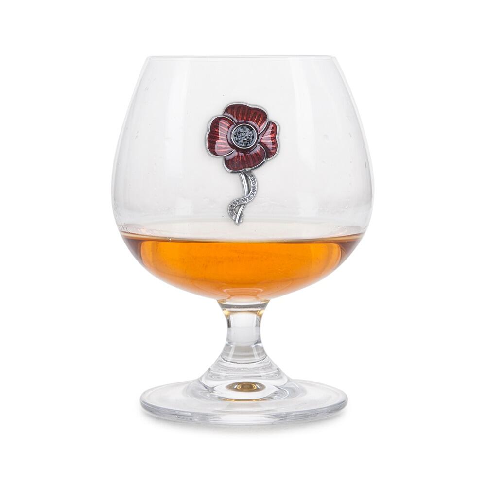 Crystal brandy glass with enamelled pewter poppy emblem and "Lest We Forget" engraving, partially filled with amber liquid