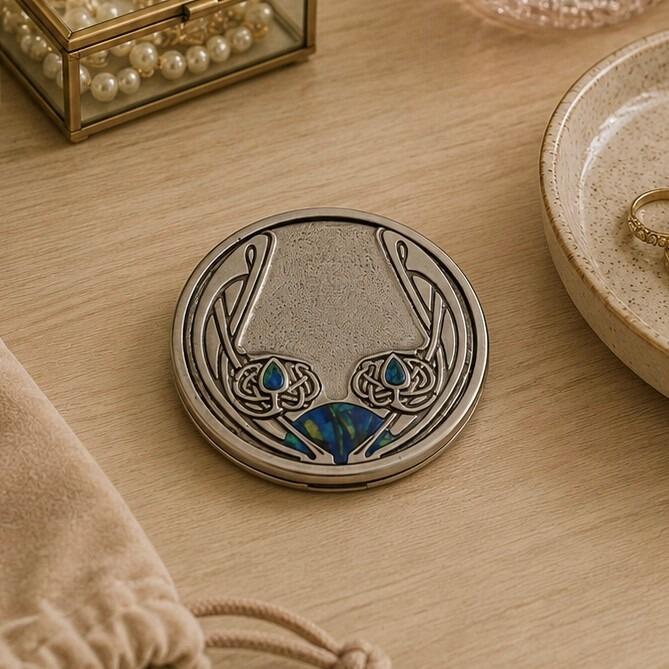 Round pewter compact purse mirror featuring an intricate Archibald Knox Art Nouveau style design with sweeping whiplash lines and vibrant blue enamel inlays