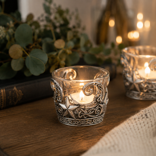 Celtic Moon and Stars pewter tealight holder with glass insert glowing on a rustic wooden table, featuring intricate knotwork and star motifs in a cosy candlelit setting
