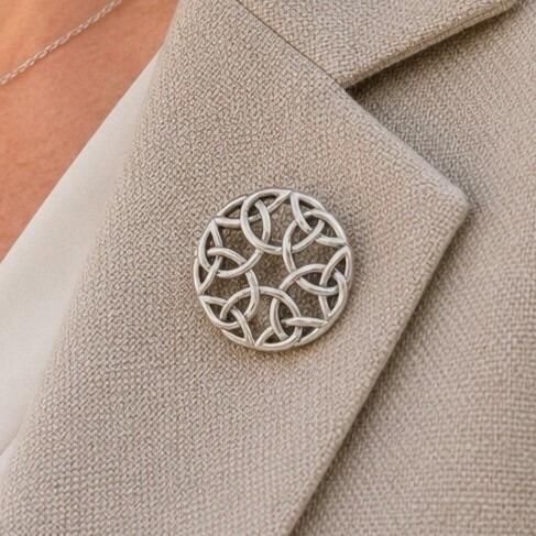 A circular pewter brooch featuring a symmetrical openwork Celtic knot design with an open center