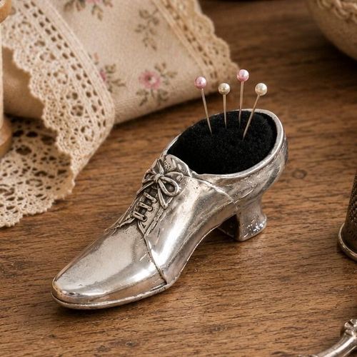 Vintage-style pewter Victorian shoe pincushion figurine with a black fabric cushion holding four pink and white pearl-head pins