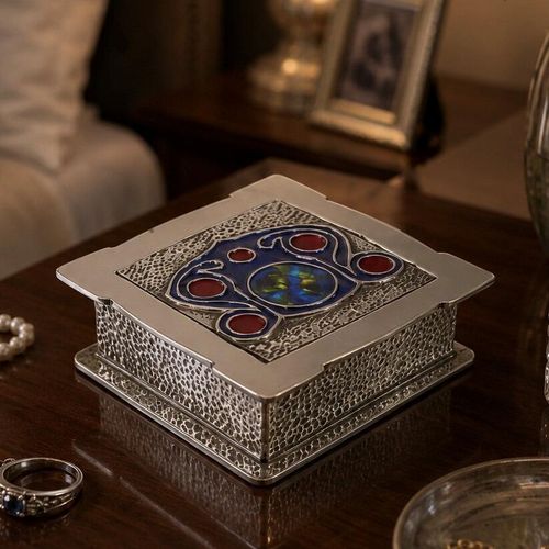 An image titled SQUARE ENAMEL ARCHIBALD KNOX BOX.jpg showing a square, polished pewter or silver-toned trinket box designed by Archibald Knox. The box features a hammered texture on its sides and lid border, with a central Art Nouveau Celtic-inspired enamel design on the lid in deep blue, vibrant turquoise, and rich red circular accents