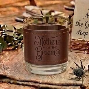 Glass tumbler wrapped in a brown stitched leather sleeve engraved with the words "Mother of the Groom" in elegant script