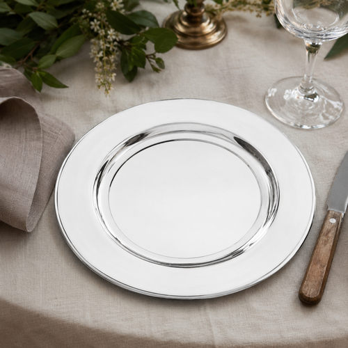 Polished 9-inch pewter plate displayed on an elegant dining table with linen tablecloth, glassware and greenery, showcasing its reflective handcrafted finish