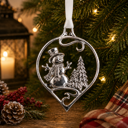 Handcrafted pewter snowman Christmas ornament featuring a cheerful snowman beside evergreen trees, hanging on a festive Christmas tree with warm holiday lights and seasonal decorations.