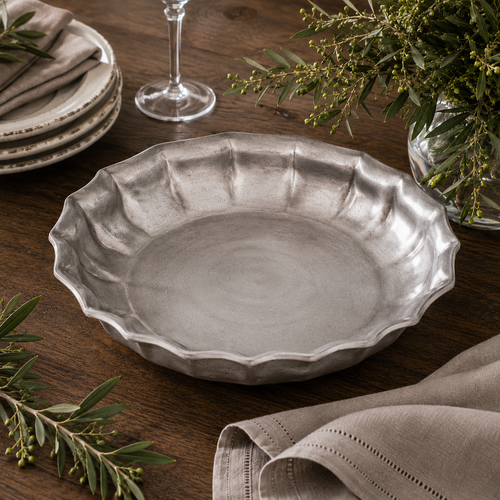 Handcrafted pewter Bavarian scalloped 8 inch bowl with a traditional satin finish, displayed as an elegant table centrepiece on a rustic wooden dining table with linen napkins, crystal glassware and decorative greenery