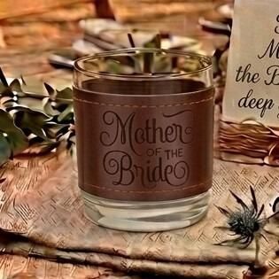 Glass tumbler wrapped in a brown stitched leather sleeve engraved with the words "Mother of the Bride" in elegant script