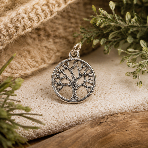 Tree of Life Pewter Charm with a loop attached on a cloth background with foliage