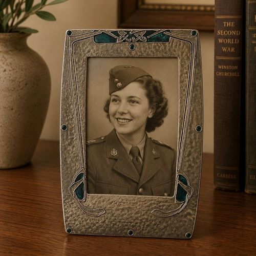 An Art Nouveau pewter picture frame with hammered texture and blue-green enamel accents, displaying a vintage black and white photograph of a smiling woman in a WWII military uniform