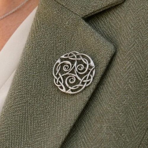 A circular pewter brooch featuring an intricate openwork Celtic triskele spiral and knotwork design