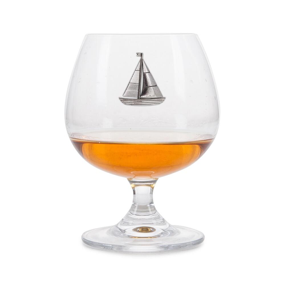 Brandy glass with handmade pewter sailing boat badge partially filled with amber spirit