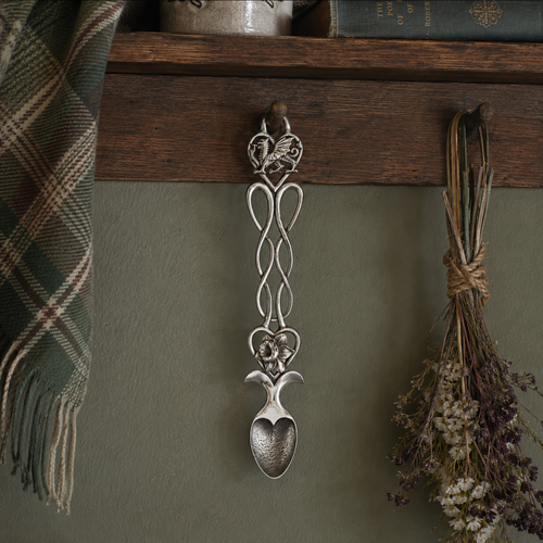 A pewter lovespoon hanging on a wood sideboard