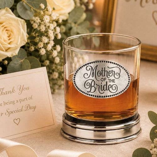 Whisky tumbler with pewter 'Mother of the Bride' badge and polished base, partially filled with amber liquid