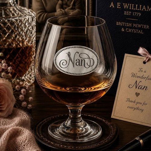 Elegant crystal brandy glass with pewter "Nan" badge, partially filled with amber liquid