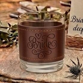 Glass tumbler wrapped in a brown stitched leather sleeve engraved with the word "Bride" and a small heart