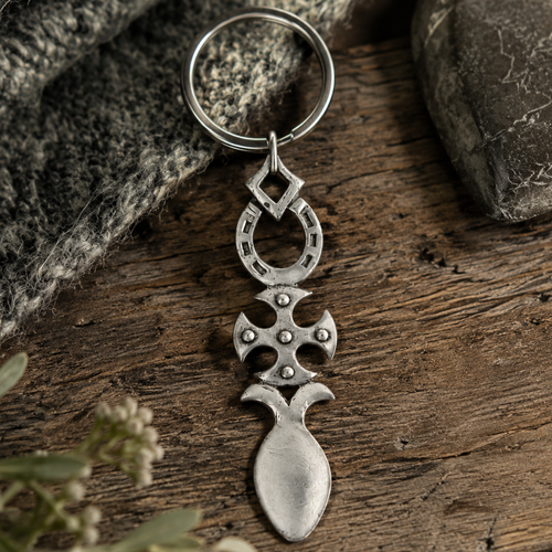Handcrafted pewter Welsh lovespoon keyring featuring an open cut-out heart and a smooth solid heart above a spoon bowl, resting on a rustic wooden background next to grey knit fabric and a smooth stone.