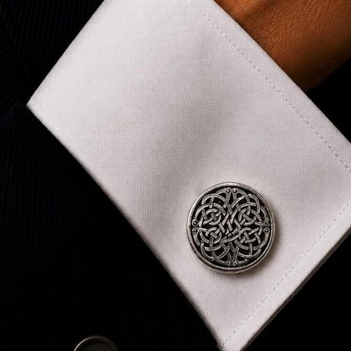 A circular pewter cufflink featuring a complex, highly detailed interwoven Celtic knotwork design with a blackened, antiqued background