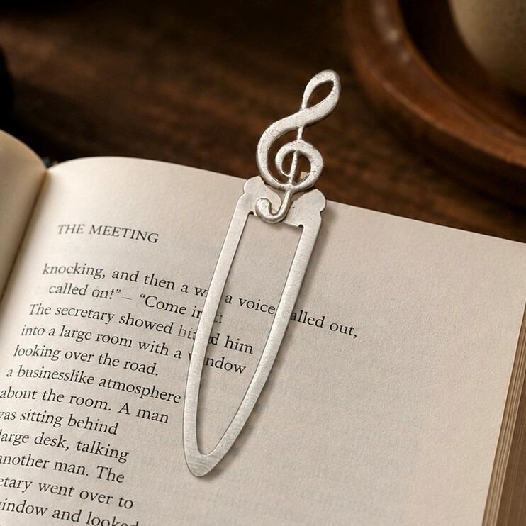 Handcrafted pewter treble clef metal clip bookmark resting on open book page