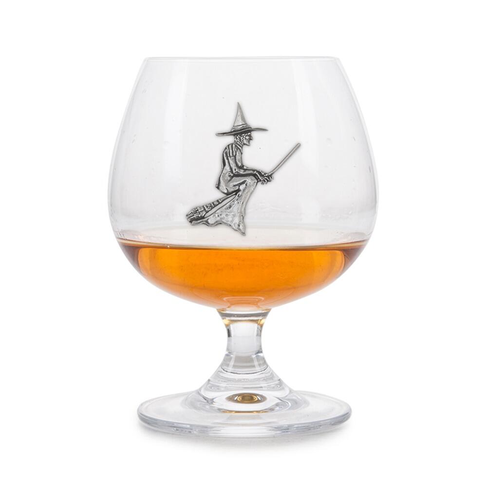 Crystal brandy glass with pewter witch emblem, partially filled with amber liquid