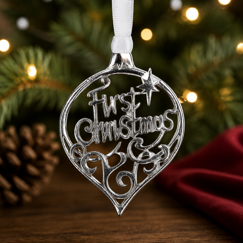First Christmas pewter tree ornament hanging in front of a decorated Christmas tree with warm festive lights and seasonal déco