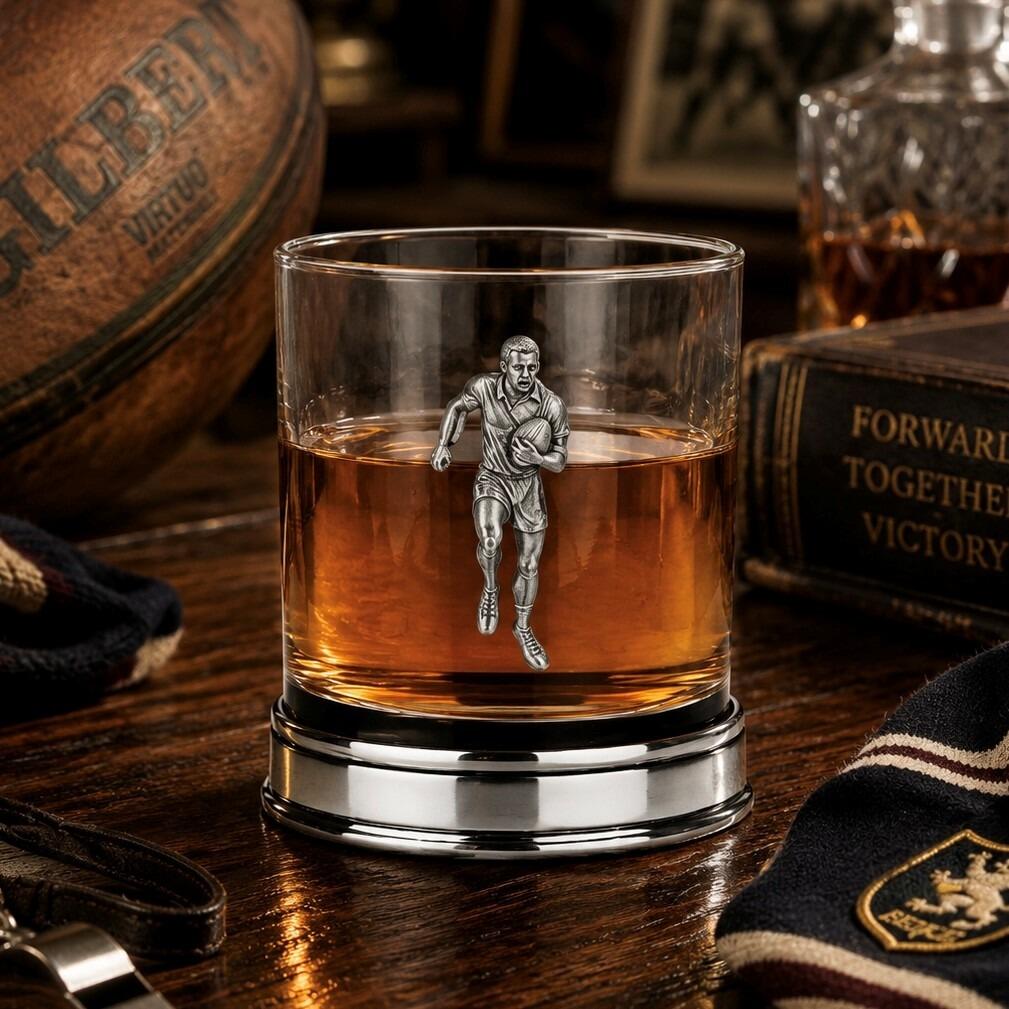 Whisky tumbler with pewter rugby player motif and polished base, partially filled with amber liquid