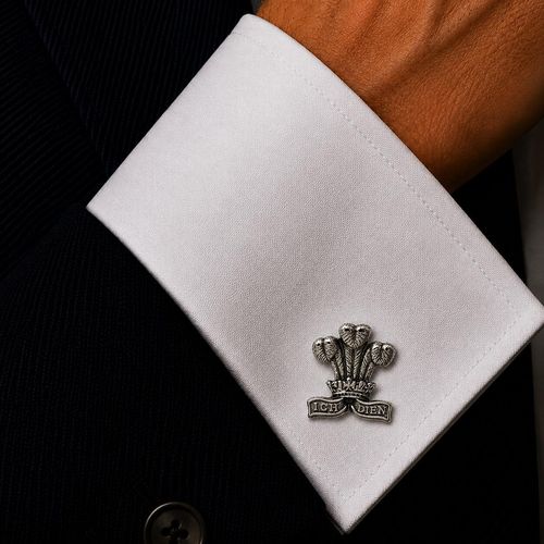 Prince of Wales feathers pewter cufflink with "Ich Dien" banner, worn on a crisp white dress shirt cuff with a dark suit jacket