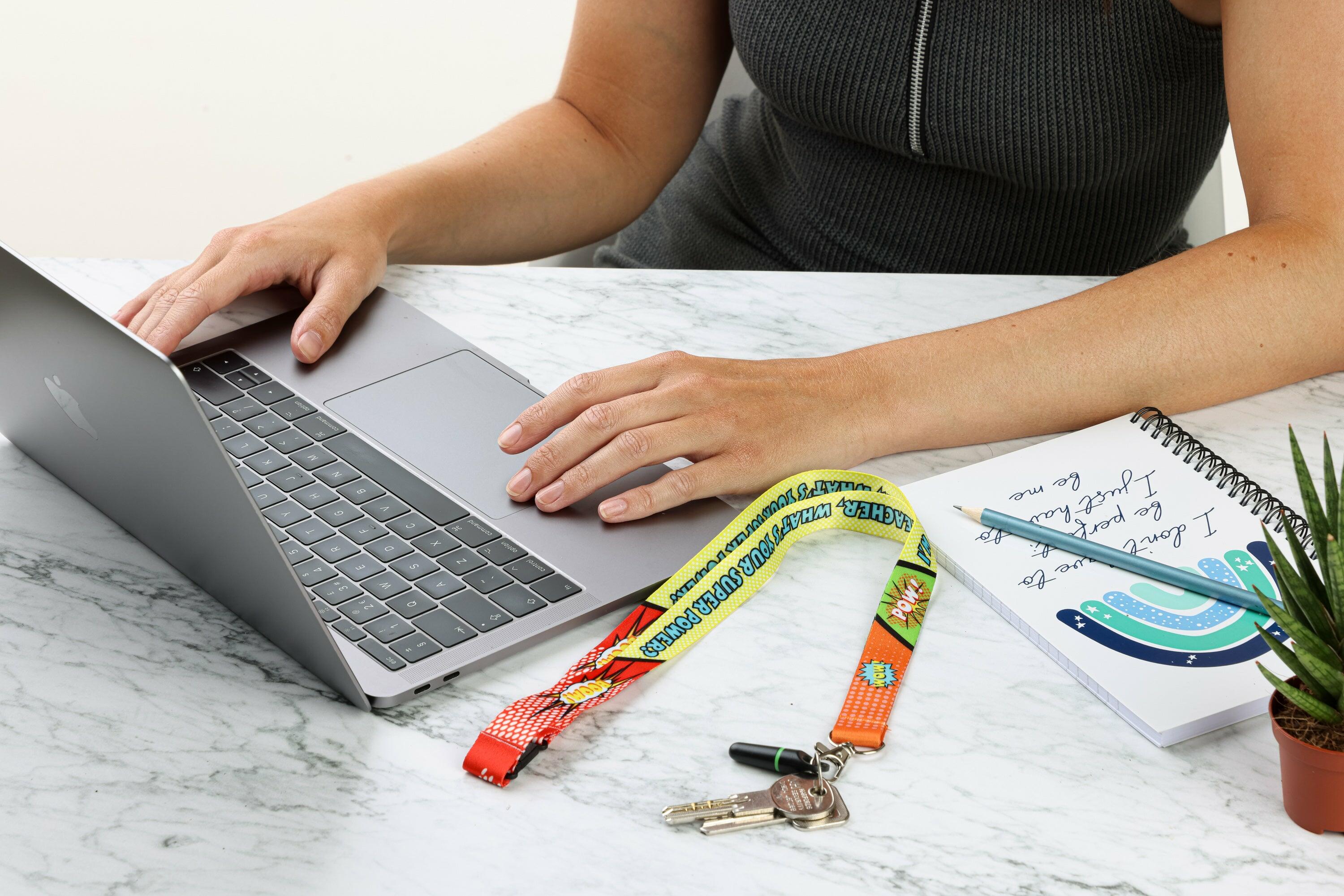 ‘I’m A Teacher, What’s Your Superpower’ lanyard placed on a desk next to a laptop, notebook, and keys
