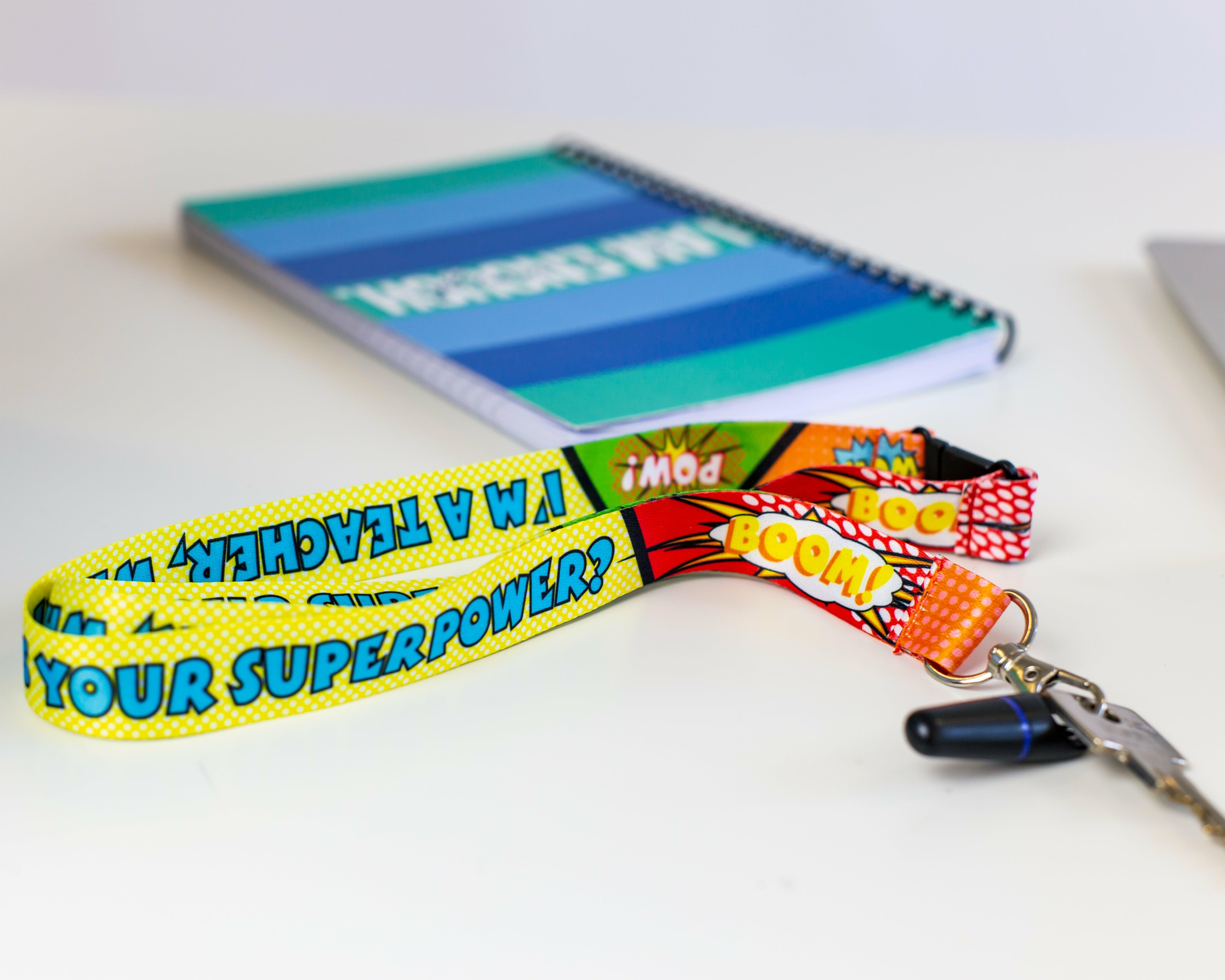 ‘I’m A Teacher, What’s Your Superpower’ lanyard laid on a desk beside a notebook and key attachment