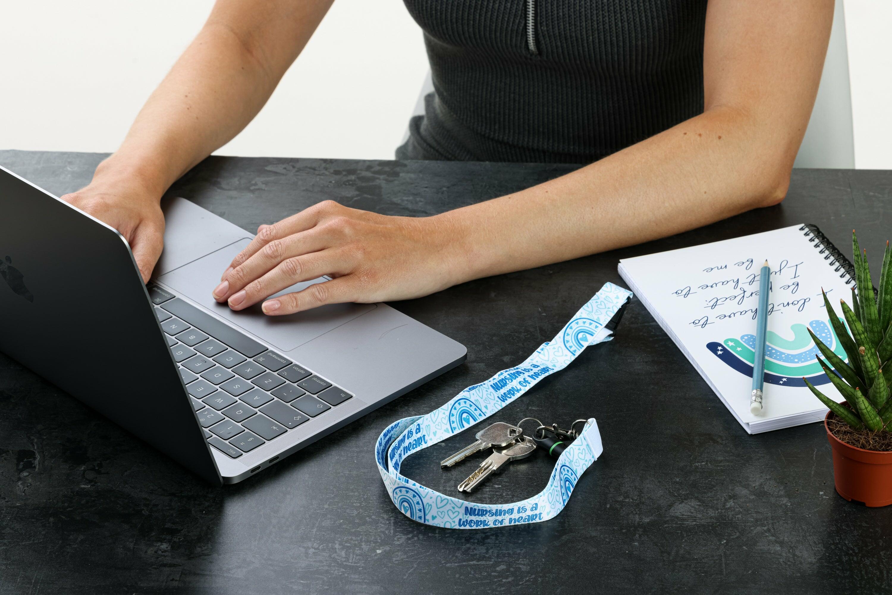 Light blue nursing lanyard with keys on desk next to laptop and notebook
