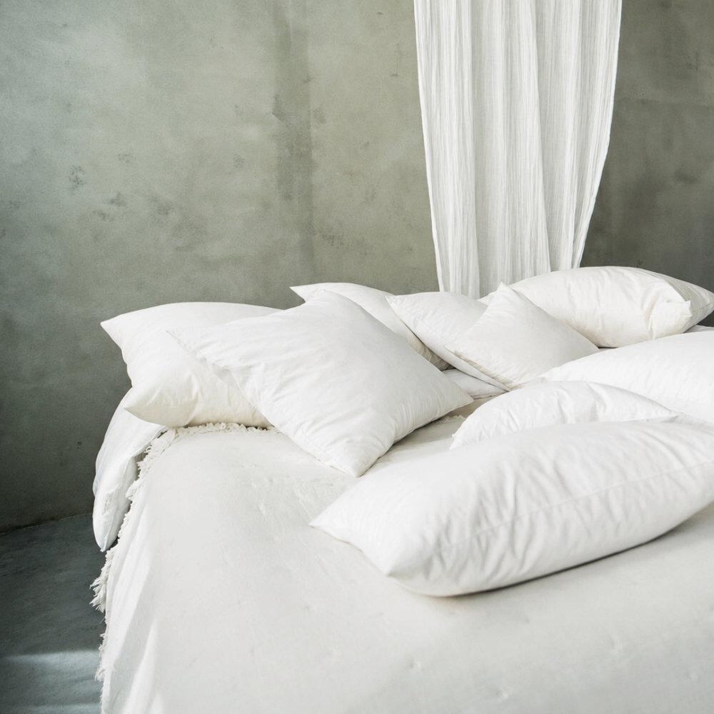 Square feather cushion inserts scattered on a bed