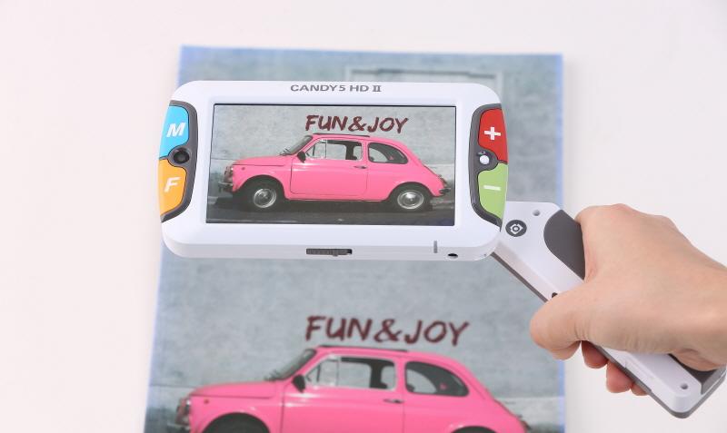 Candy 5 magnifying an image of a pink car the words fun and joy can be seen on the wall behind the car